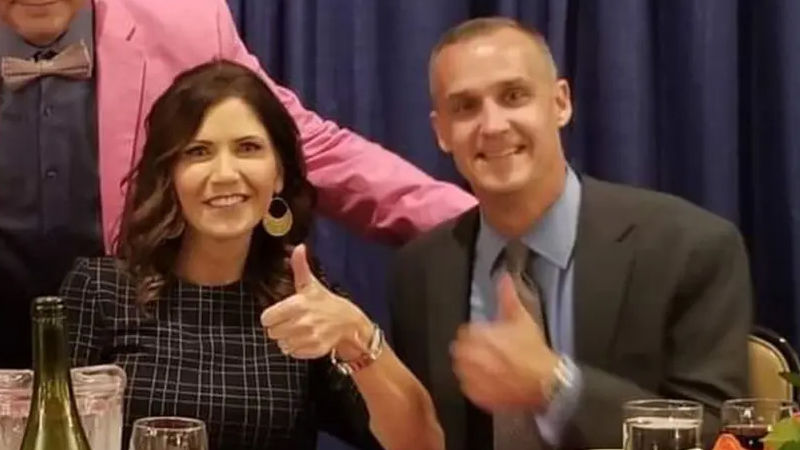 Kristi Noem and Corey Lewandowski are giving thumbs up at a dinner together